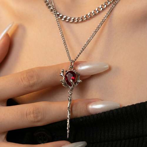 Close-up of a silver necklace with a red gemstone worn by a person.